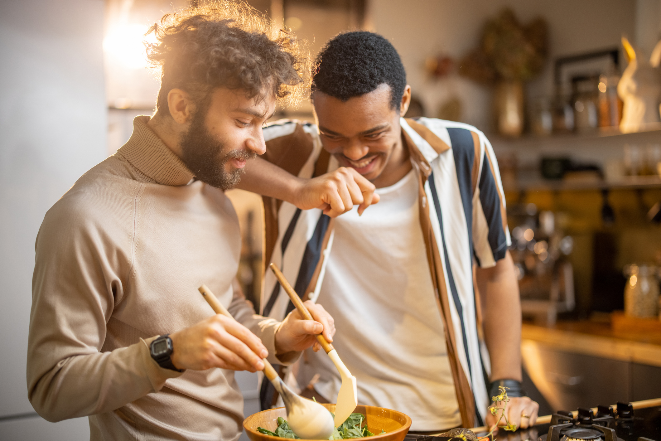 Two guys having fun while making salad together in kitchen